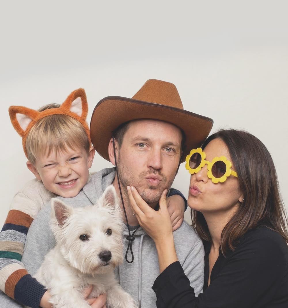 A family posing with props and their dog in PhotoDA's Classic Room, a soft neutral backdrop